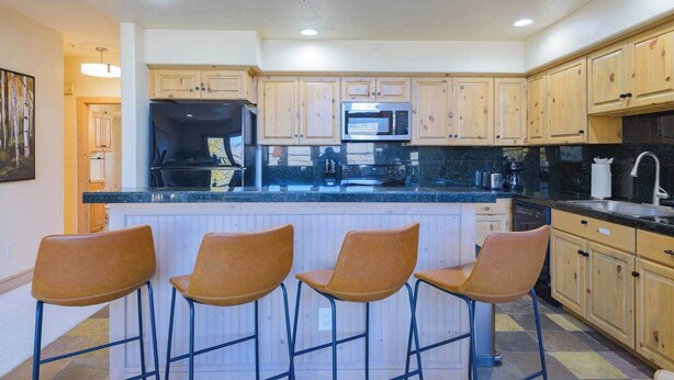 A kitchen with wooden cabinets, a black countertop, and three bar stools. - Updated Treasury Point condo, garage, hot tub! (Crested Butte)