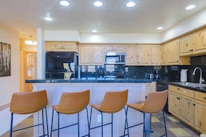 A kitchen with wooden cabinets, a black countertop, and three bar stools. - Updated Treasury Point condo, garage, hot tub! (Crested Butte)