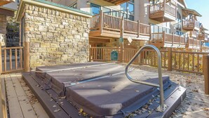 A stone exterior wall, a wooden deck, and a hot tub area with steps and railings. - Updated Treasury Point condo, garage, hot tub! (Crested Butte)