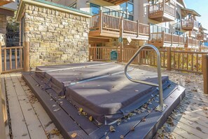 A stone exterior wall, a wooden deck, and a hot tub area with steps and railings. - Updated Treasury Point condo, garage, hot tub! (Crested Butte)