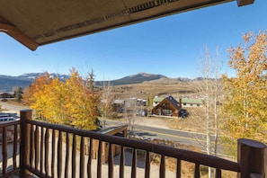 A wooden balcony overlooking a mountain landscape with autumn-colored trees and a view of a lodge. - Updated Treasury Point condo, garage, hot tub! (Crested Butte)
