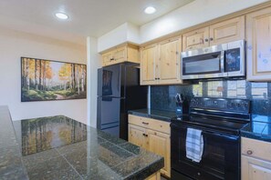 A kitchen with wooden cabinets, a black refrigerator, a microwave, and a stove. - Updated Treasury Point condo, garage, hot tub! (Crested Butte)