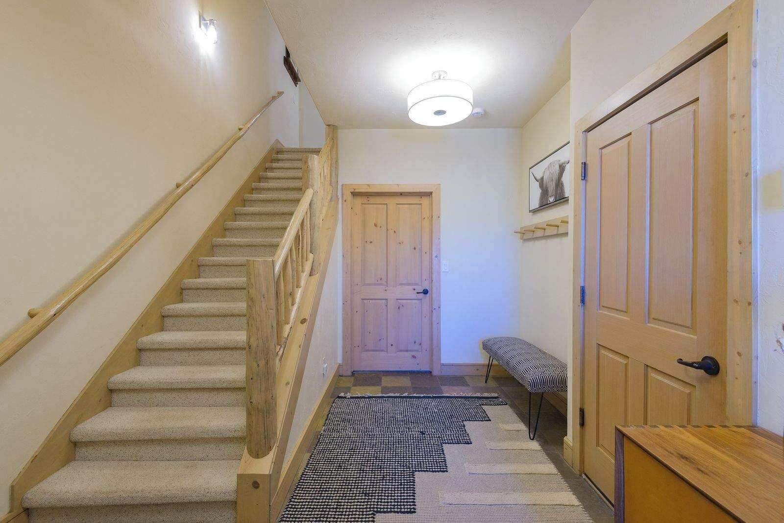 A staircase with wooden handrails, carpeted steps, and a patterned rug at the bottom.