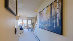 A hallway with a large painting of trees, a white sofa, and a dining area with a table and chairs. - Updated Treasury Point condo, garage, hot tub! (Crested Butte)