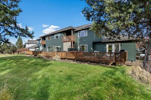 A two-story townhouse with a wooden deck, a fenced backyard, and a clear blue sky. - New! Eagle Crest Retreat | 3BR Townhome w/ Resort Access—Pet Friendly (Redmond)
