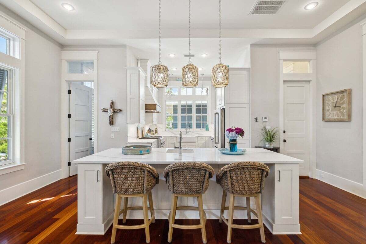 A spacious kitchen with a large island, white cabinetry, and three wicker bar stools.