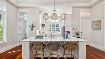 A spacious kitchen with a large island, white cabinetry, and three wicker bar stools.