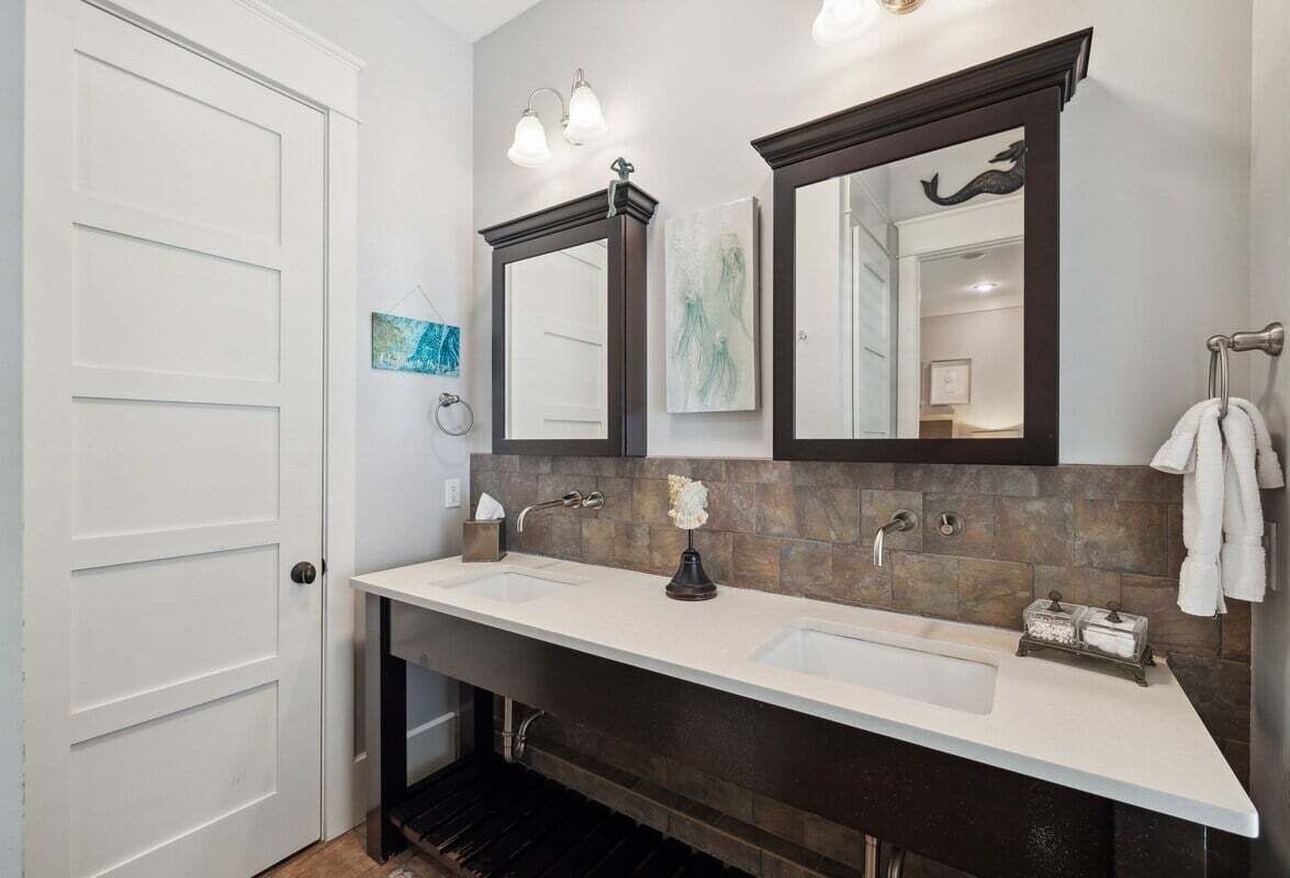 A bathroom with a double sink, two mirrors, a towel rack, and a small vase.