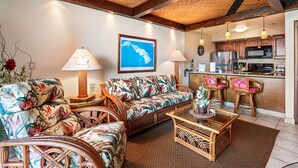 A living room with a sofa, chairs, a coffee table, and a kitchen area with a microwave and refrigerator. - Easy Walk to Town Ocean Front AC & Wifi - Vrkcv (Kailua-Kona)