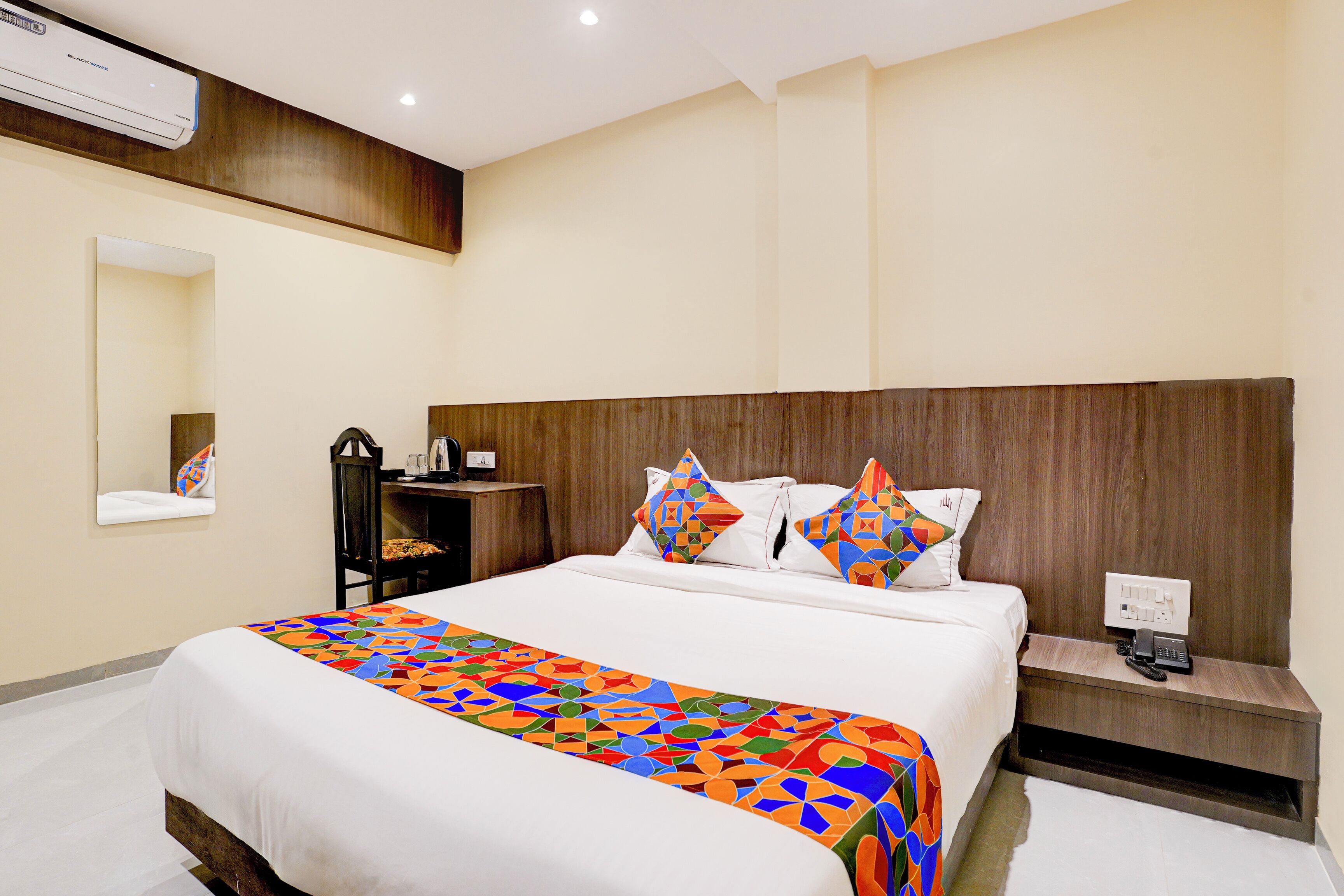Habitación de hotel con una cama grande, una mesita de noche con teléfono, un espejo y aire acondicionado de pared.