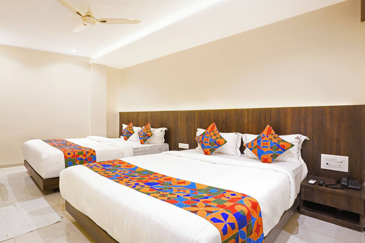 A hotel room with three beds, a ceiling fan, a wooden headboard, a bedside table with a phone, and a power outlet.