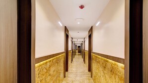 Un largo y estrecho pasillo con suelo de mármol y columnas de madera, que conduce a una puerta al final.