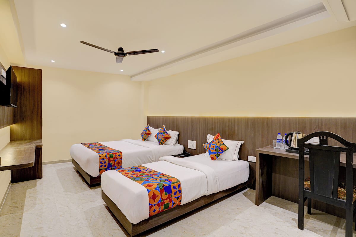 A hotel room with two beds, a desk, a chair, a ceiling fan, and a TV.