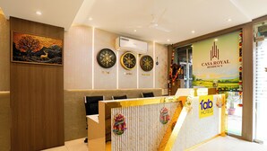 Zona de recepción de un hotel, con mostrador, relojes de pared y un cartel grande con un paisaje.