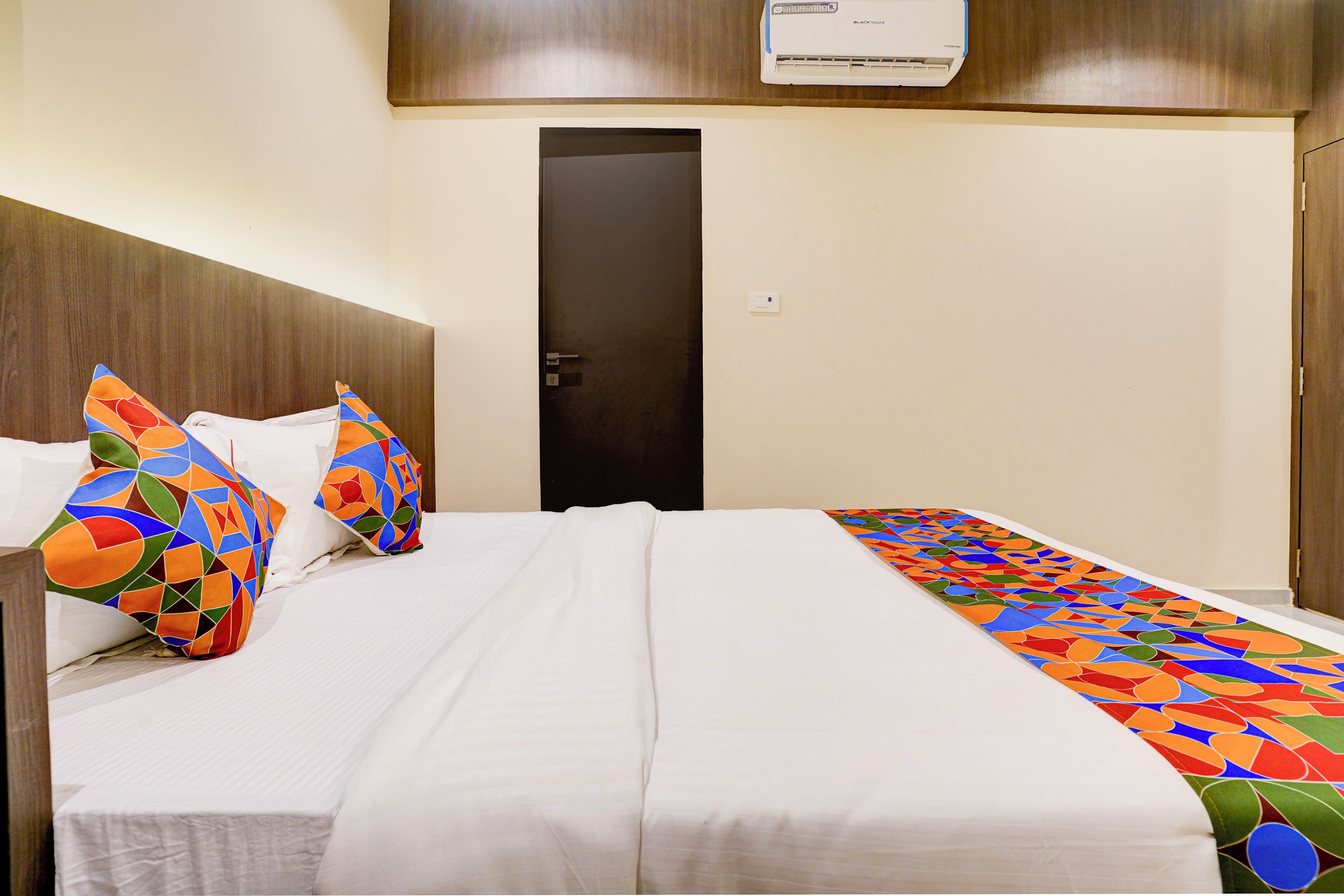 Habitación de hotel con cama, almohadas, una puerta y un equipo de aire acondicionado.