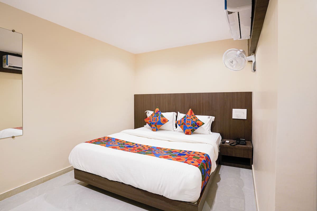 A hotel room with a bed, a nightstand, a bedside table, a wall-mounted fan, and a mirror.