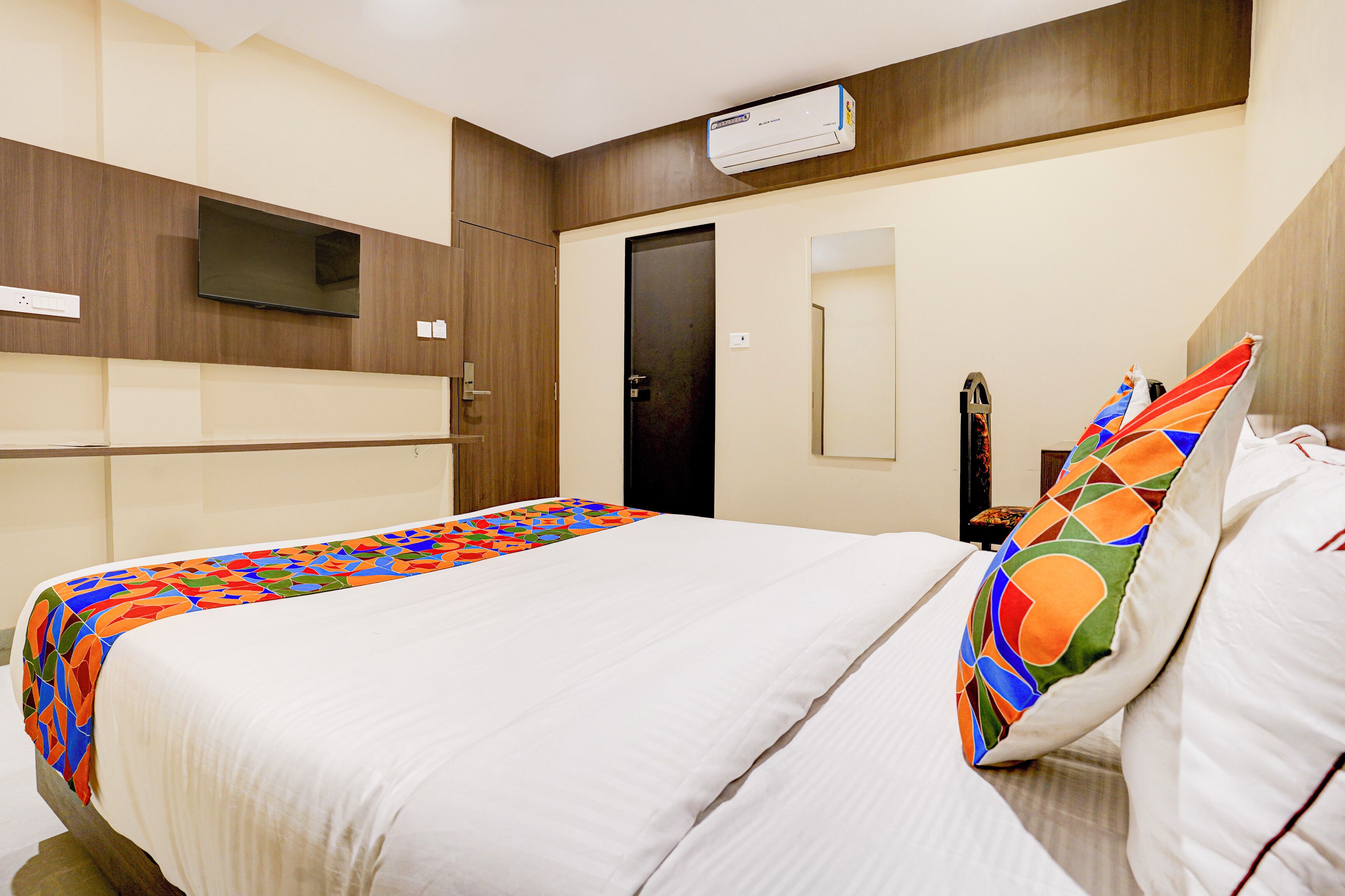 Una habitación de hotel con cama, televisor, aire acondicionado y una puerta.