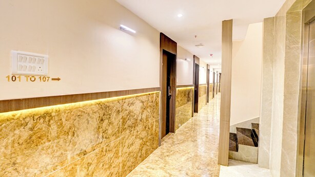 Un pasillo de hotel con suelo de mármol, puertas numeradas del 101 al 107 y una escalera.
