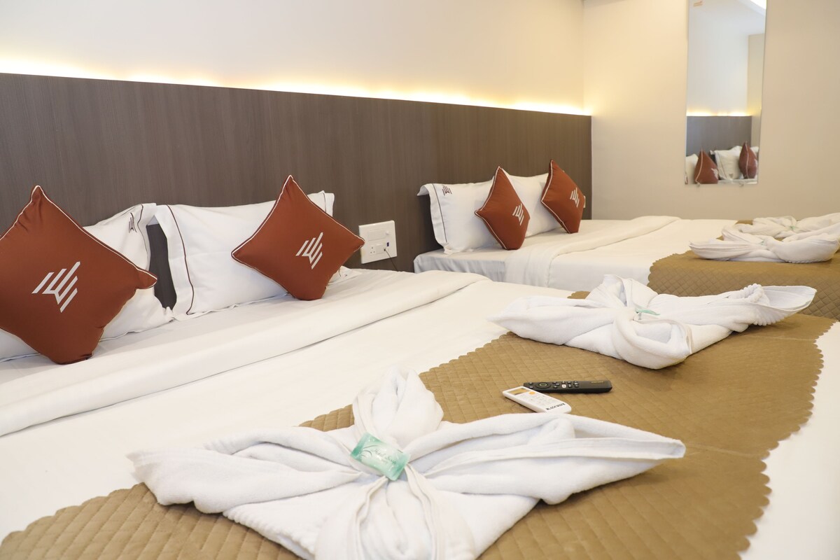 A hotel room with two beds, each with white linens and brown pillows, and a remote control on the bed.