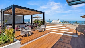 Una terrazza panoramica sul tetto con posti a sedere all'aperto, un pergolato e vista sull'oceano.
