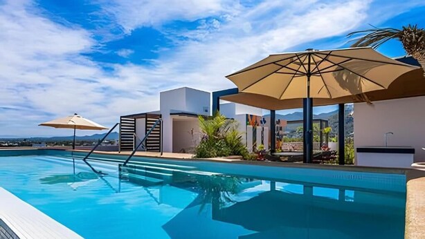 Una piscina con acqua cristallina e azzurra, circondata da architettura moderna e ombreggiata da grandi ombrelloni.