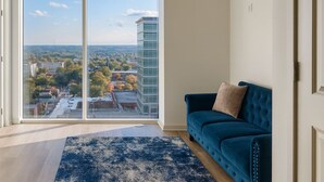 A modern living room with a large sliding glass door leading to a city view, a blue sofa, and a patterned rug. - Cozy 1-bedroom apartment with AC in marvelous Raleigh (Raleigh)