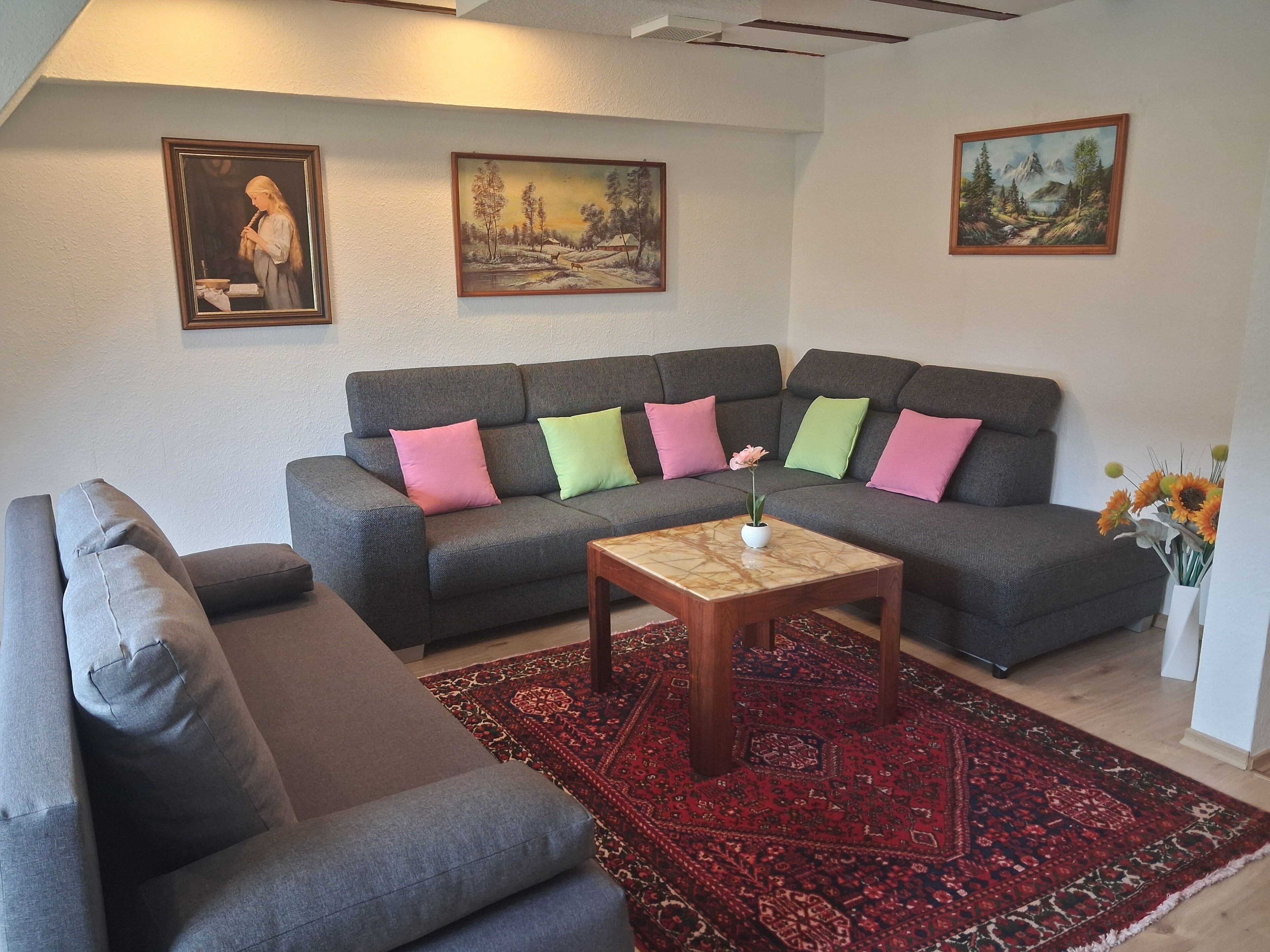 Een woonkamer met een grijze modulaire bank, een klein houten bijzettafeltje en een rood tapijtblek.
