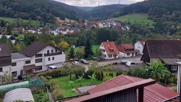 Zona residencial com casas, um campo verde e turbinas eólicas ao fundo.