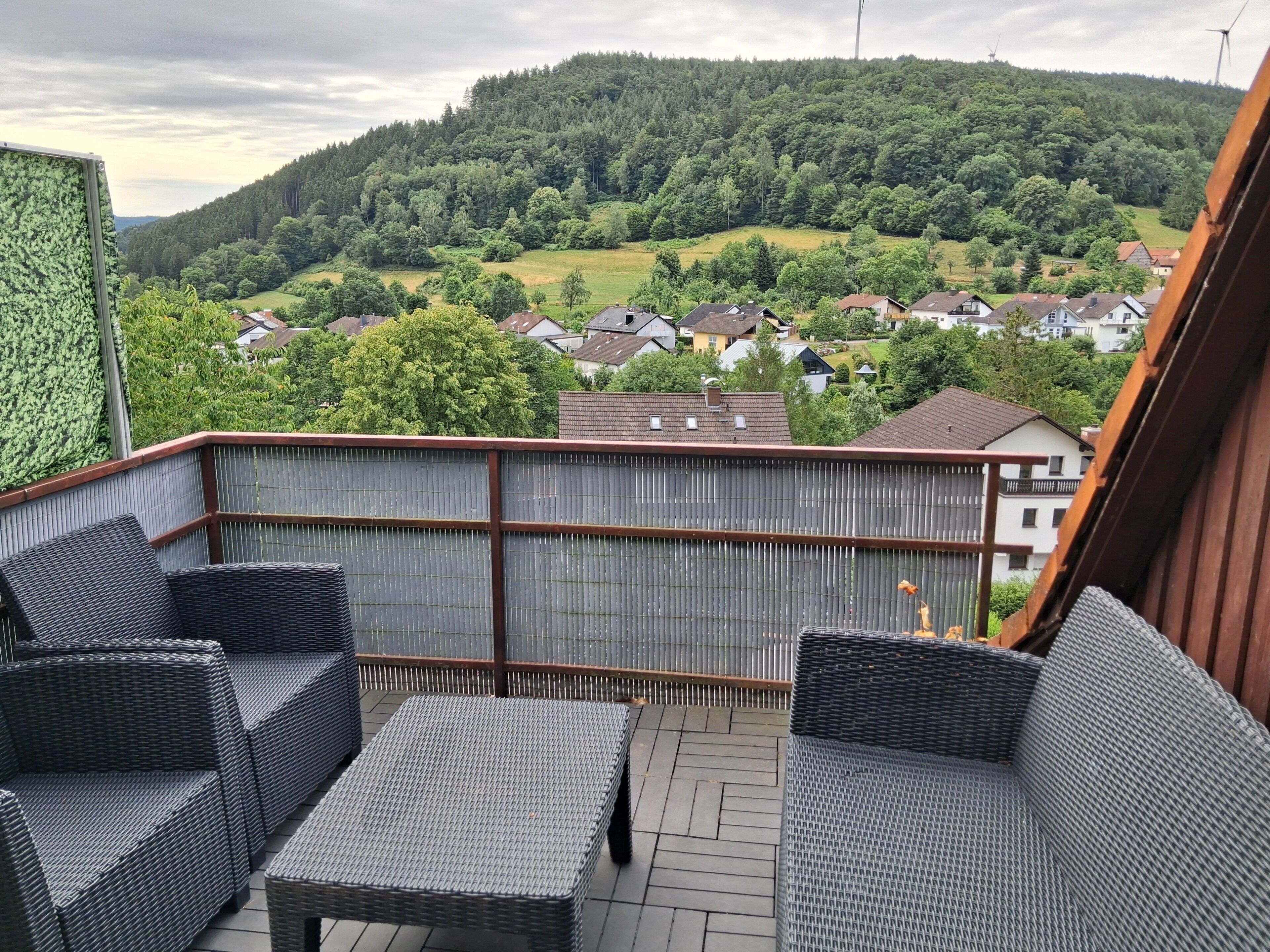 Een balkon met rieten meubilair, met uitzicht op een woonwijk en heuvels.