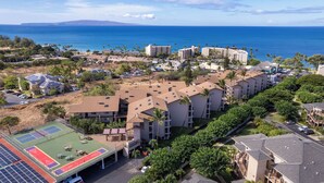 Un resort con diversi edifici, un campo da tennis e vista sull'oceano.