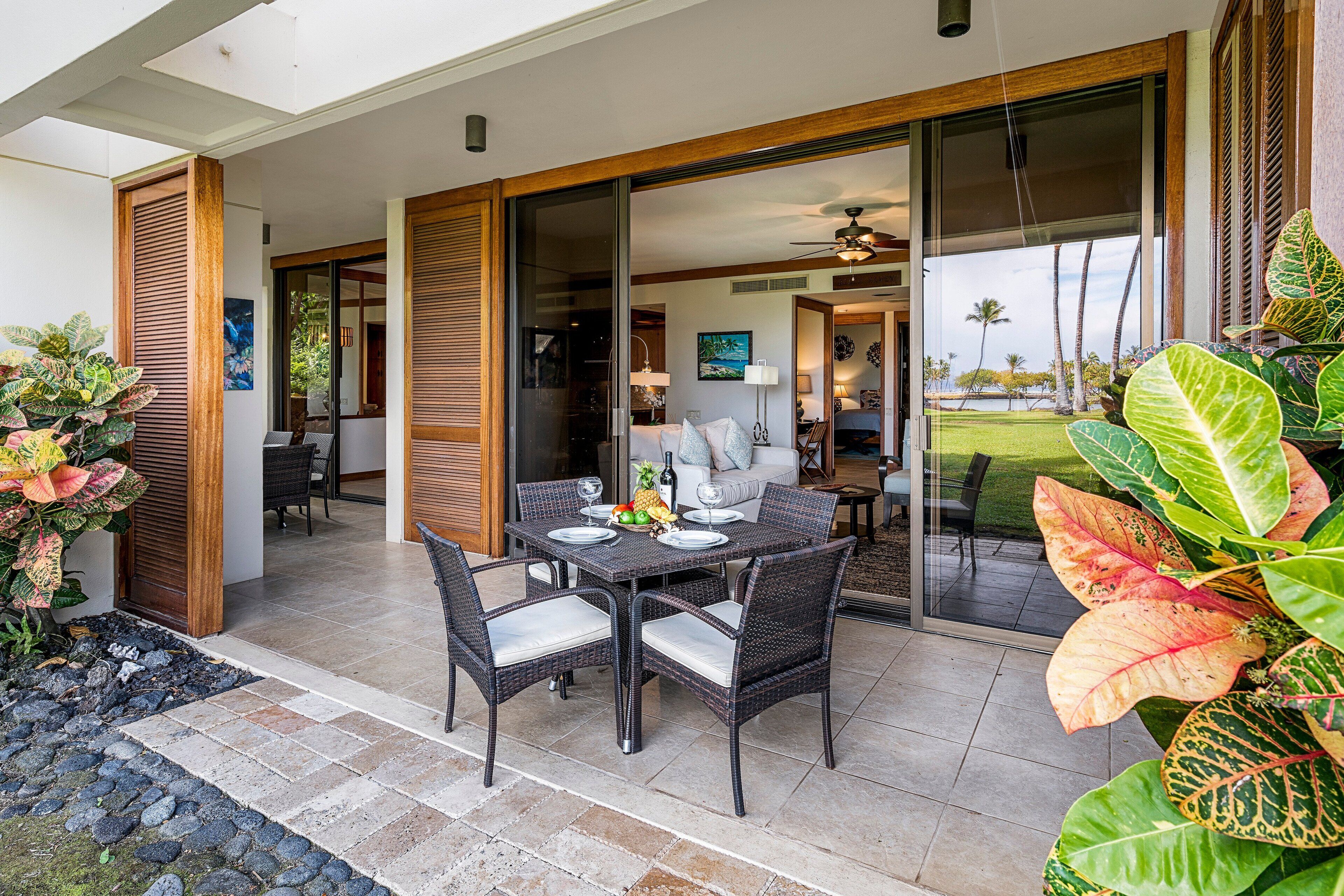 An outdoor dining area with a table set for four, surrounded by wicker chairs with cushioned seats.