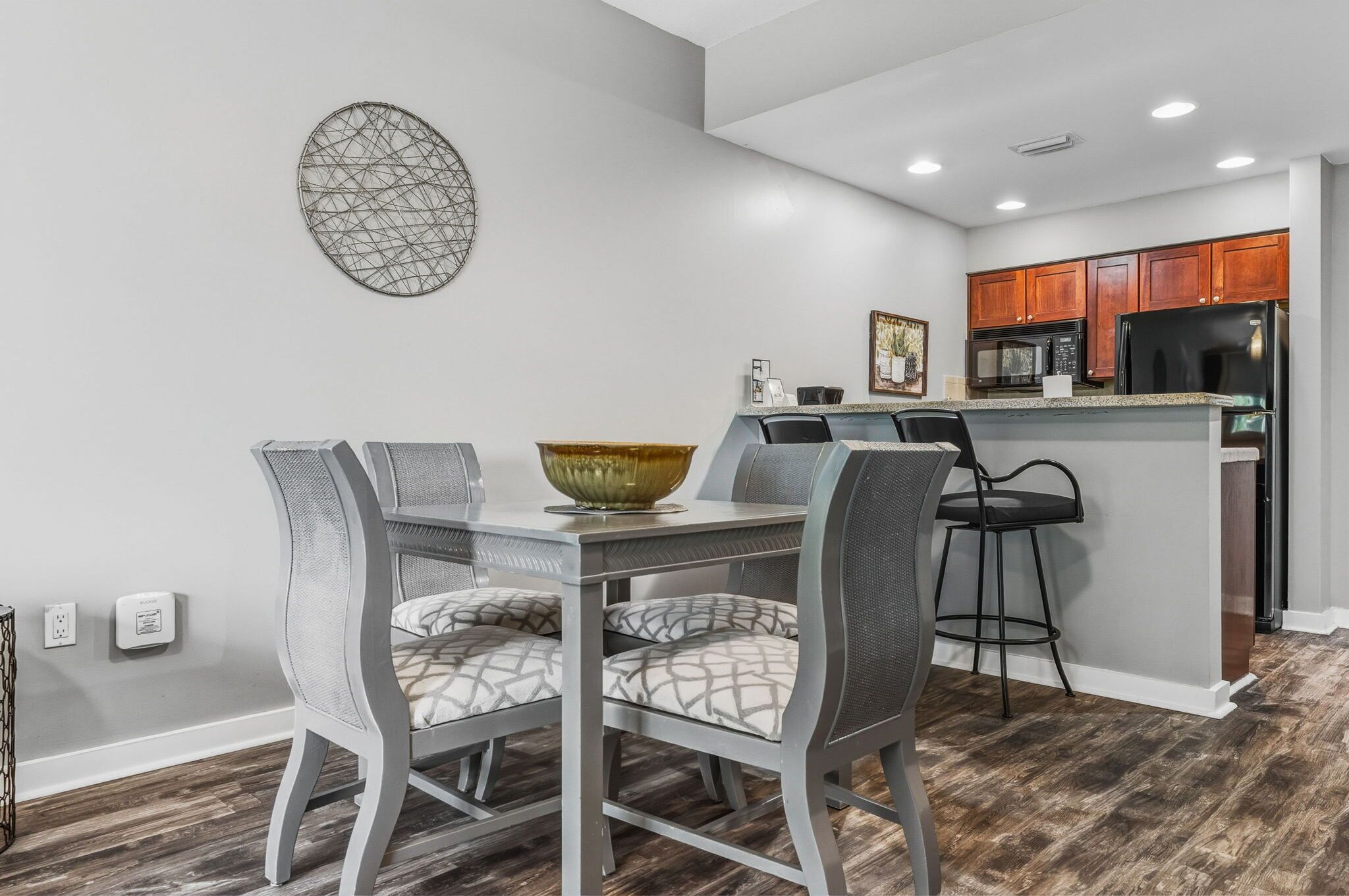 A modern kitchen with a dining area, featuring a granite countertop, stainless steel appliances, and a decorative wall piece.