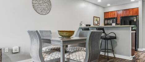 A modern kitchen with a dining area, featuring a granite countertop, stainless steel appliances, and a decorative wall piece.