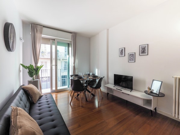 A modern living room with a black sofa, dining table, chairs, a TV, and a potted plant. - A Chic Getaway in Milan—Porta Venezia (Milano)