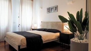 Una camera da letto con un letto, comodini, una pianta in vaso e quadri appesi al muro.