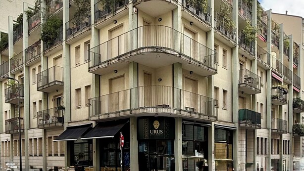 Un edificio a più piani con balconi, un negozio e un attraversamento pedonale.