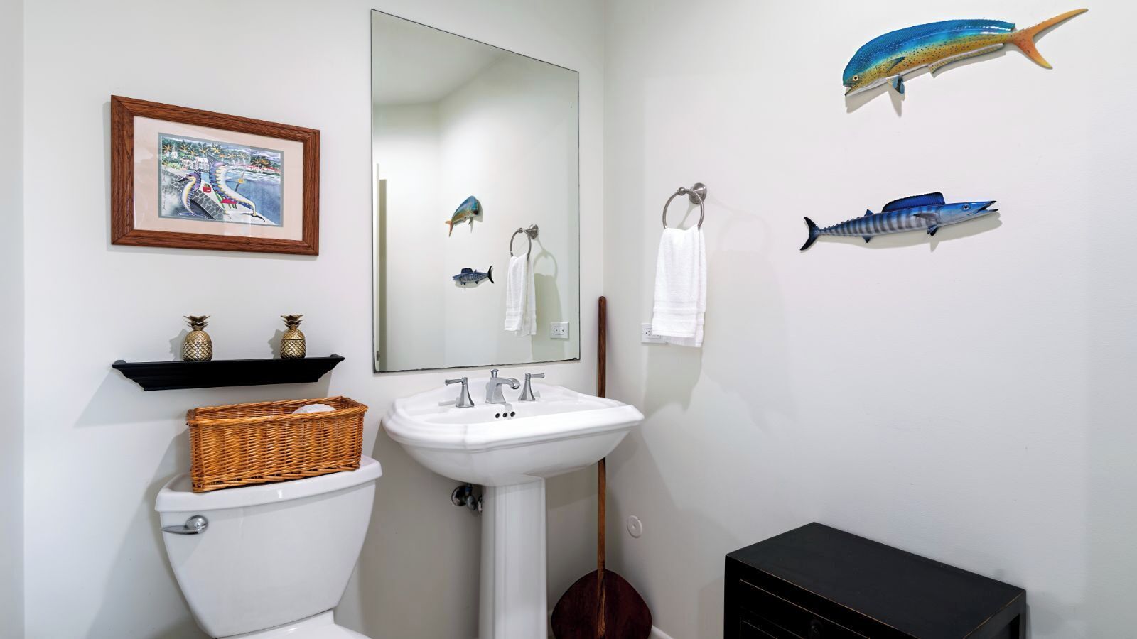 A bathroom with a white sink, a mirror, a toilet, and a black cabinet. There are two fish decorations on the wall.