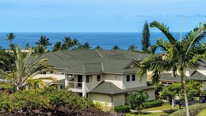 A two-story house with a balcony, surrounded by tropical vegetation and a view of the ocean. - Updated Townhome Ocean View Private BBQ & Lanai - Vrkcv (Kailua-Kona)