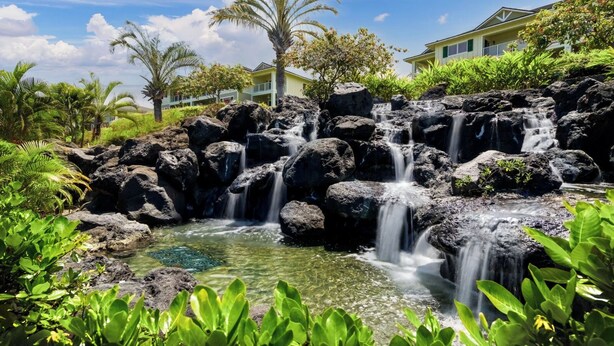 A natural rock waterfall with clear water, surrounded by lush greenery and a building in the background. - Updated Townhome Ocean View Private BBQ & Lanai - Vrkcv (Kailua-Kona)