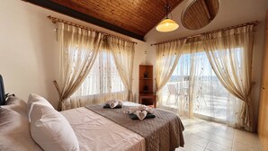 Ein Schlafzimmer mit zwei Betten, einer Holzbalkendecke und Meerblick durch große Fenster.