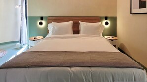 Ein ordentlich bezogenes Bett mit Holz-Kopfteil, zwei Nachttischen und Wandleuchten.