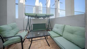 Un balcon avec un canapé vert, une petite table et un siège suspendu.