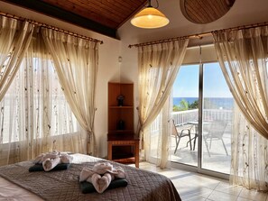 Ein Hotelzimmer mit Bett, einem Holzregal mit einer Vase und einem Balkon mit Meerblick.