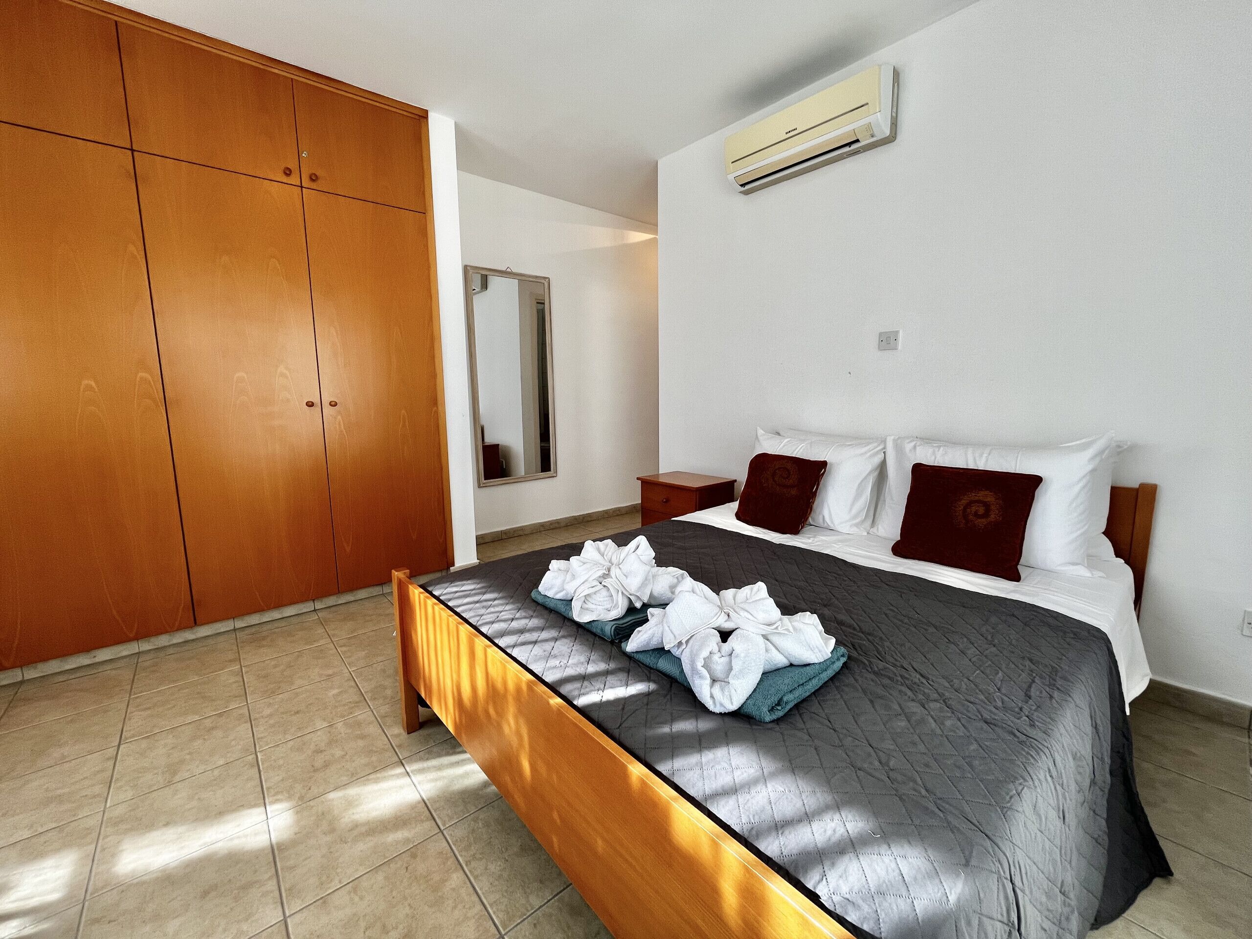 Una habitación de hotel con una cama grande, un armario, un espejo y un equipo de aire acondicionado.