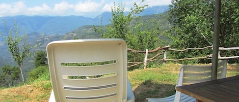 A patio with two white plastic chairs and a table, overlooking a mountainous landscape.