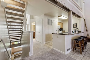 A modern kitchen with a central island, bar stools, and a staircase leading to an upper level. - Embers & Evergreens Retreat Hot tubs Pool LLV457 (South Lake Tahoe)