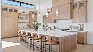 Een moderne keuken met een groot eiland, barstoelen, houten kastjes en hanglampen.