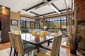 A spacious dining area with a large wooden table and striped chairs, a cozy seating area with sofas and a fireplace, and large windows offering a view of a mountainous landscape. - Ski-in/Ski-out Luxury 3-Bedroom Retreat at Flagstaff Lodge! Epic Views, Hot Tub! (Park City)