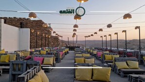 A rooftop restaurant with outdoor seating, stone walls, and hanging lights.