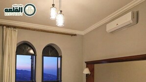 A hotel room with a bed, two windows with views, an air conditioning unit, and a lamp.
